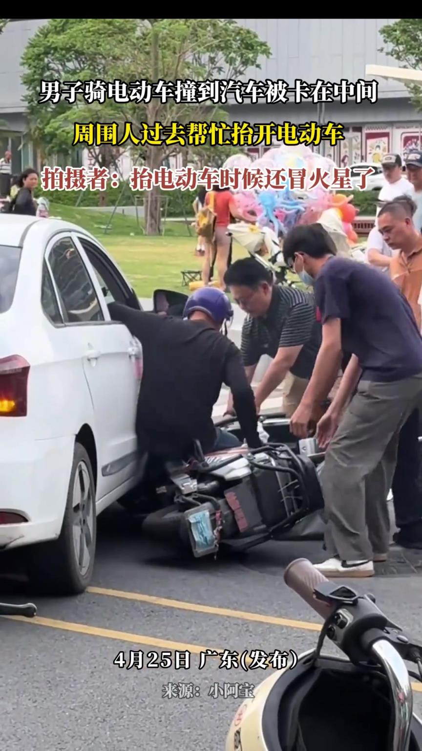 男子騎電動(dòng)車撞到汽車被卡在中間，周圍人過(guò)去幫忙抬開(kāi)電動(dòng)車
