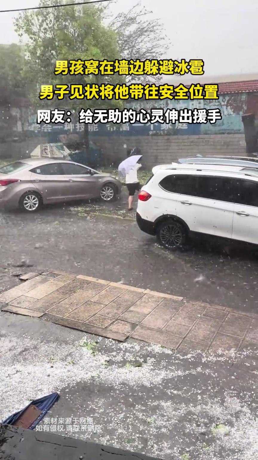 男孩窝在墙边躲避冰雹，男子见状将他带往安全位置