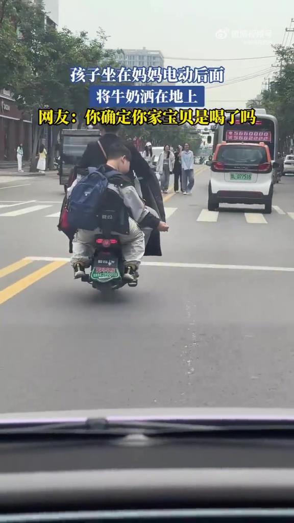 孩子坐在妈妈电动后面 将牛奶洒在地上