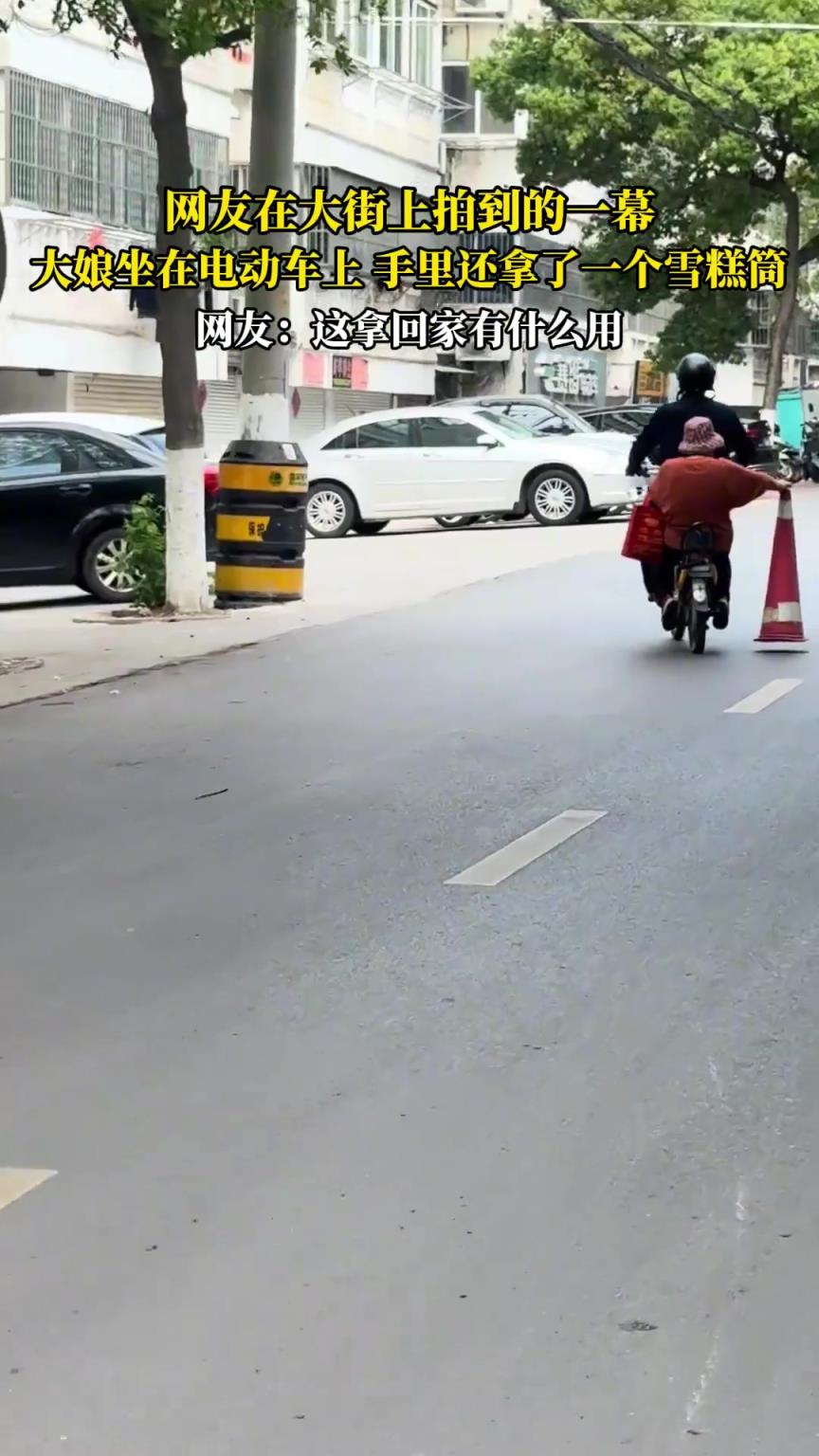 網(wǎng)友在大街上拍到的一幕，大娘坐在電動車上，手里還拿一個雪糕筒