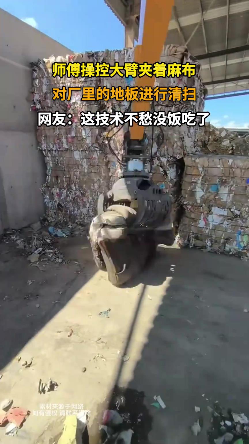 师傅操控大臂夹着麻布，对厂里的地板进行清扫