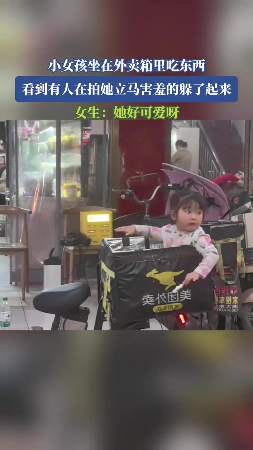 小女孩坐在外卖箱里吃东西，看到有人在拍她立马害羞的躲了起来