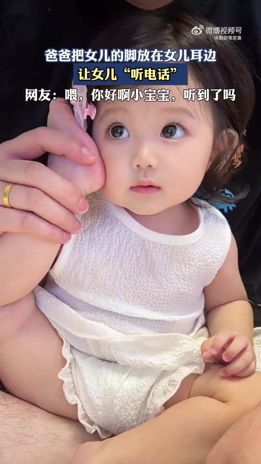 爸爸將女兒的腳放其耳邊，讓女兒“聽電話”