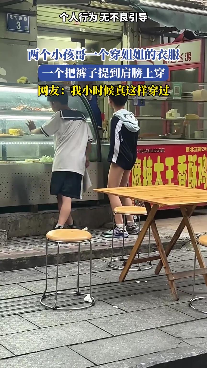 两个小孩哥一个穿姐姐的衣服，一个把裤子提到肩膀上穿