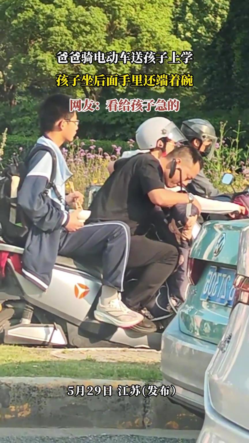 爸爸騎電動車送孩子上學(xué)，孩子坐后面手里還端著碗