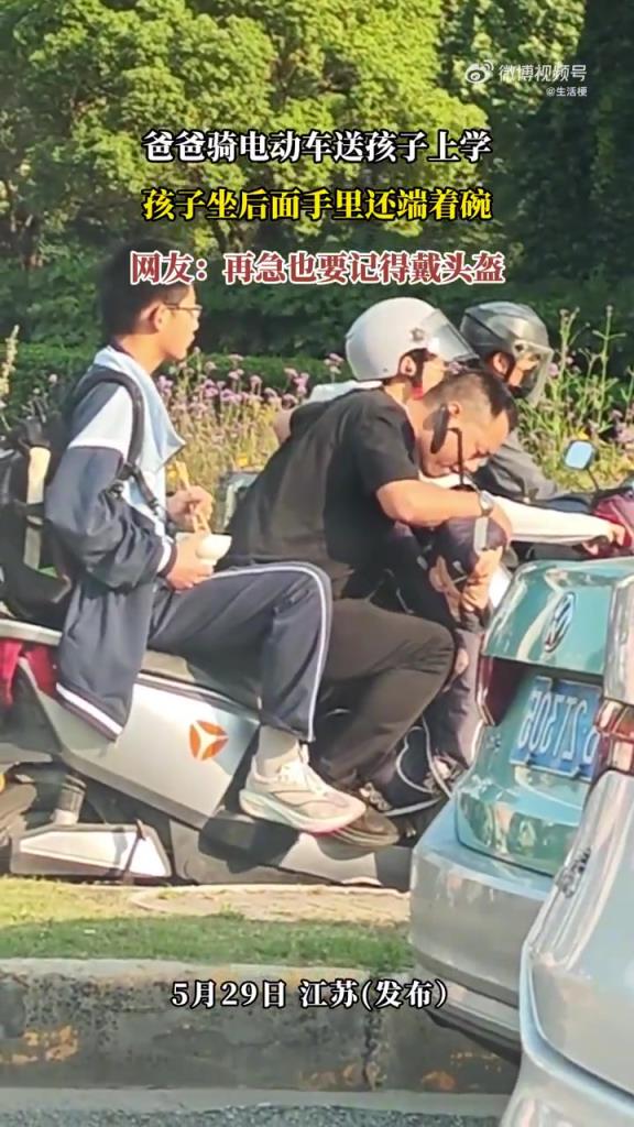 爸爸騎電動(dòng)車(chē)送孩子上學(xué) 孩子坐后面手里還端著碗