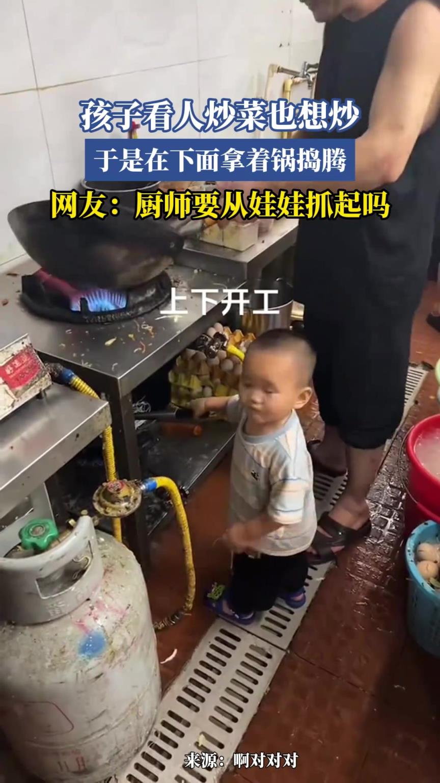 孩子看人炒菜也想炒，于是在下面拿著鍋倒騰
