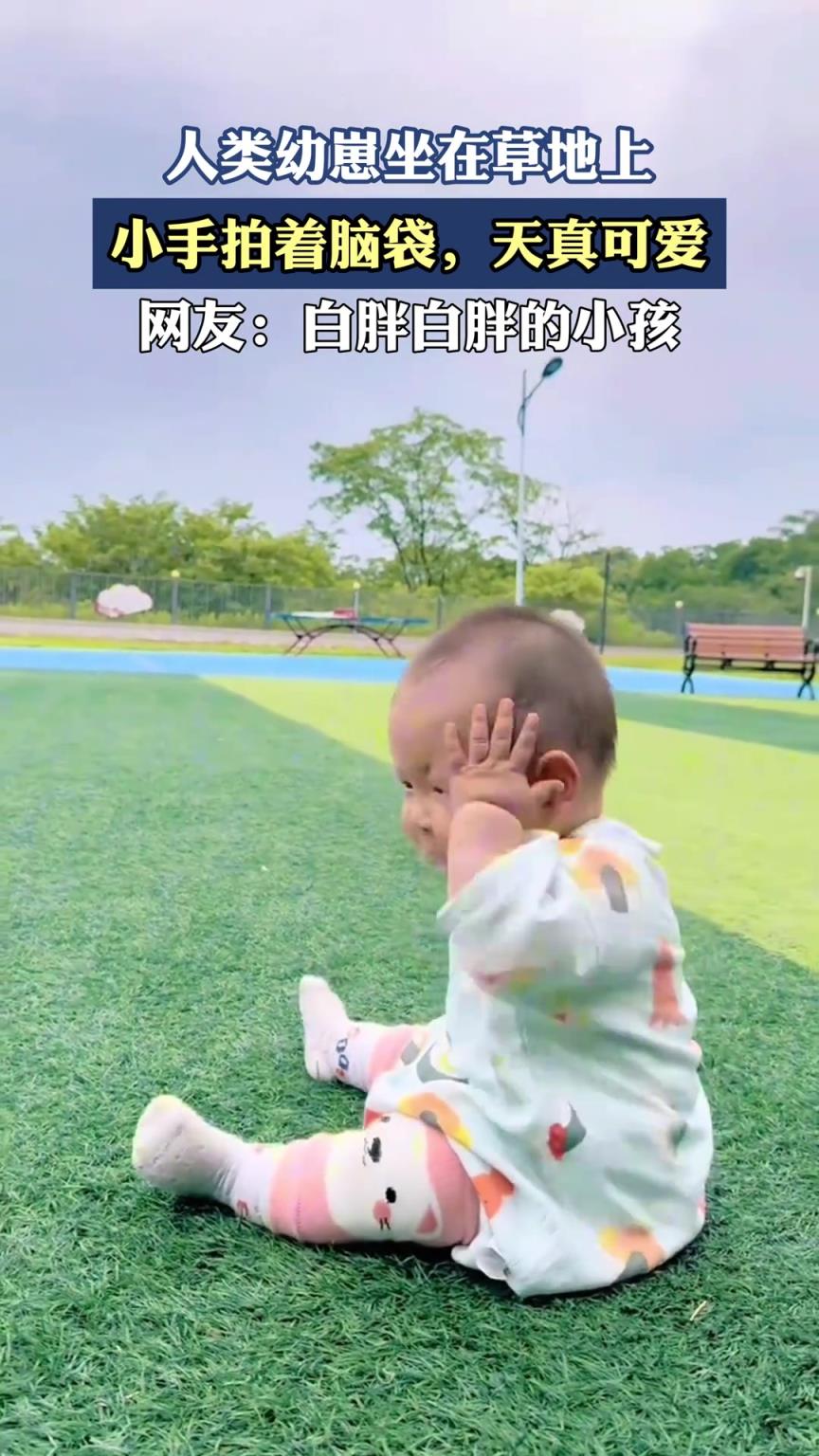 人類幼崽坐在草地上，小手拍著腦袋，天真可愛